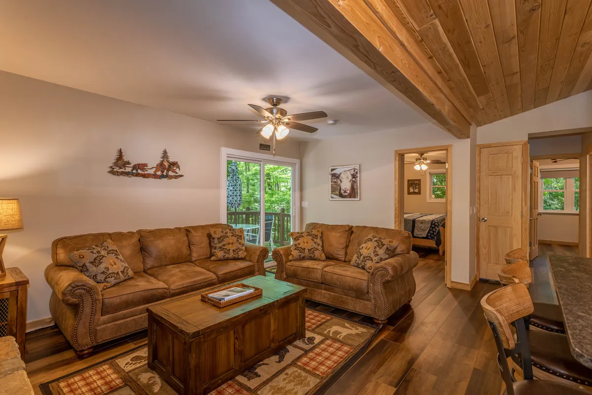 A sunlit living room with comfortable sofas, a rustic coffee table, and large windows offering a picturesque outdoor view. The space feels airy and inviting, ideal for sunny mornings, relaxed afternoon chats, or festive family celebrations.