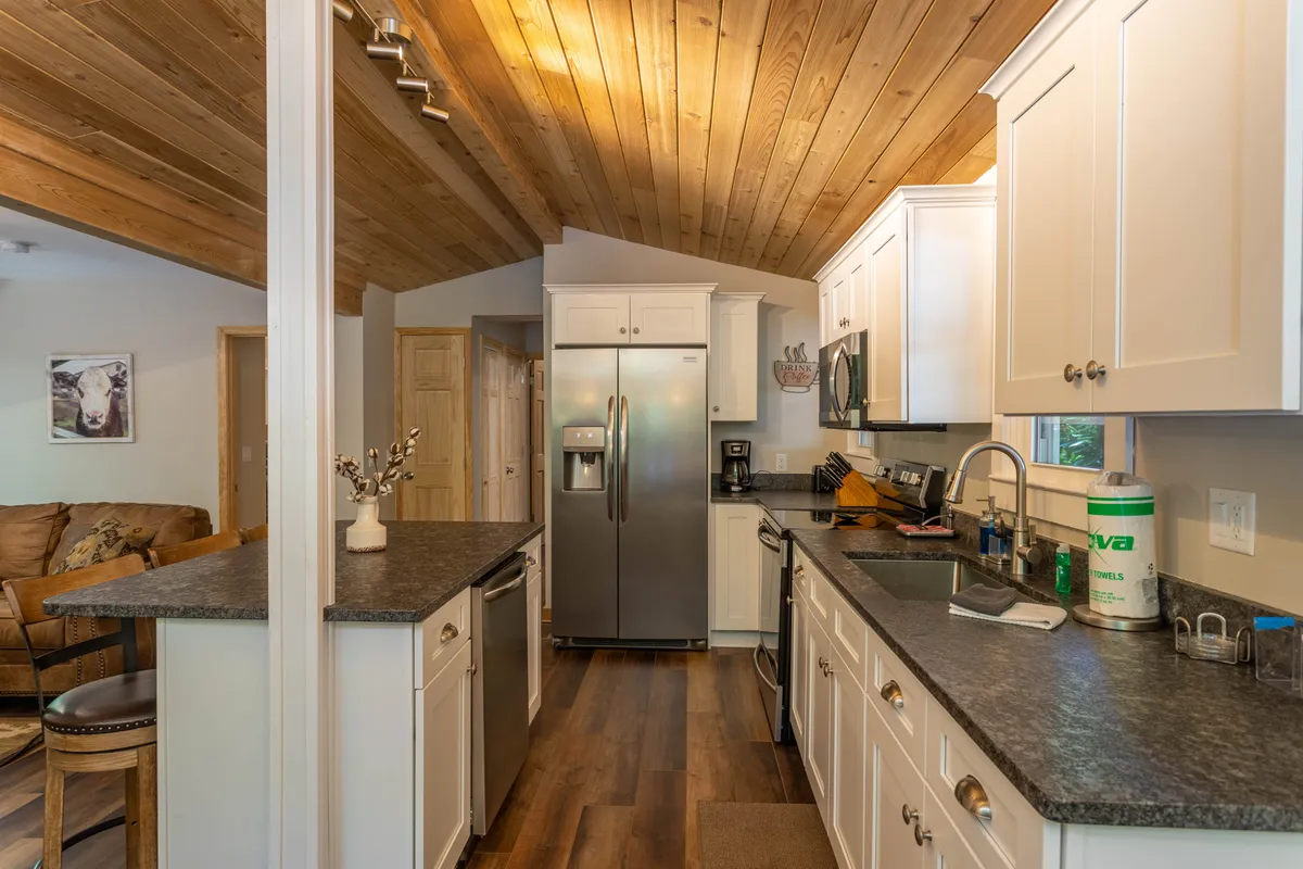 A warmly lit kitchen and living space with a prominent kitchen island, sleek stainless steel appliances, wooden ceiling beams, and comfortable seating arranged for conversation. The space feels inviting and well-suited for groups to gather, share meals, or plan their next adventure.