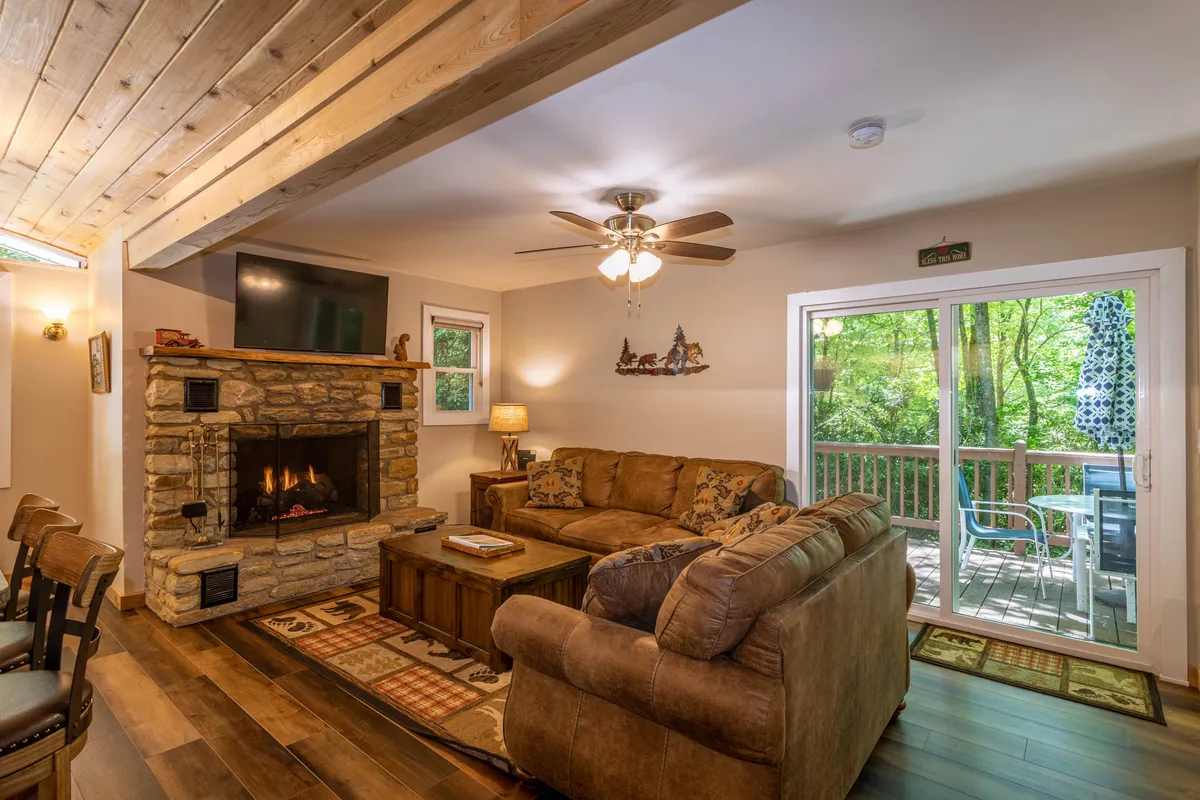 A warm and inviting living room featuring a beautiful stone fireplace, a comfy sofa, and expansive windows that open to the outdoor deck. The scene exudes comfort and is perfect for couples unwinding after a day of exploration.