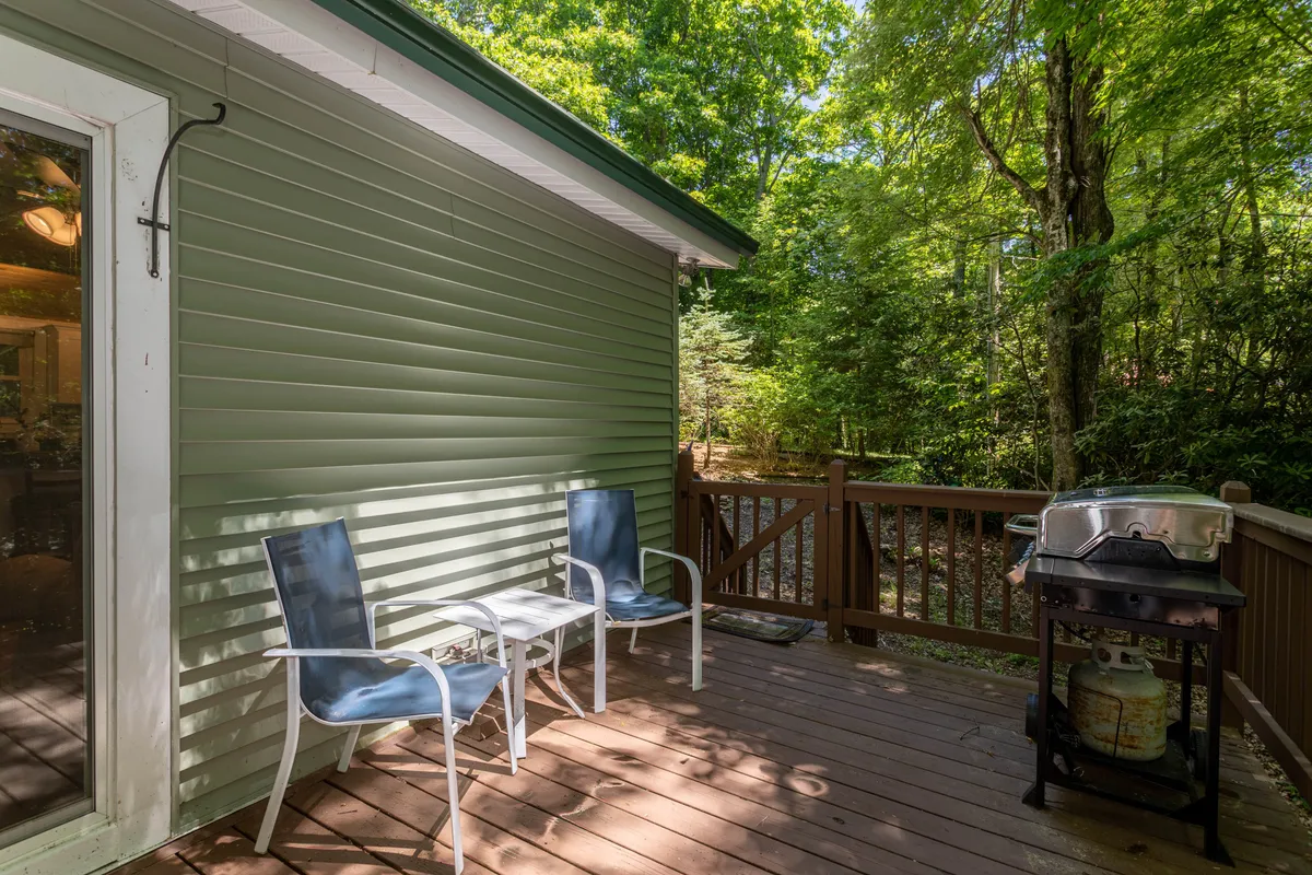 The image shows a wooden deck with two chairs, a grill, and lush trees in the background. The setting evokes a relaxing and inviting atmosphere, perfect for outdoor family activities or unwinding together after a day of local adventures.