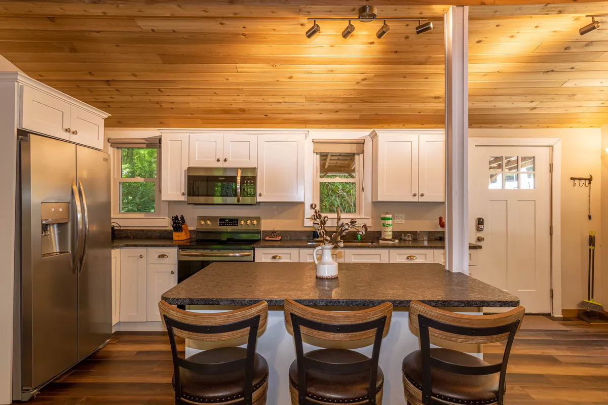 A beautifully updated kitchen with a spacious island, stainless steel appliances, white cabinetry, and a wooden ceiling, all under soft, welcoming light. This kitchen visually communicates both the modern upgrades and the warmth alluded to in the narrative. It’s a space clearly designed for family gatherings, casual meals, and joyful cooking experiences.