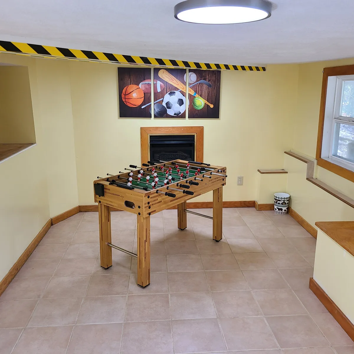 Here, the focal point is a foosball table set in a cozy, sport-themed basement room. A fireplace offers a sense of warmth, while the playful wall art and seating create a casual, friendly vibe suited to group gaming sessions and post-adventure relaxation.
