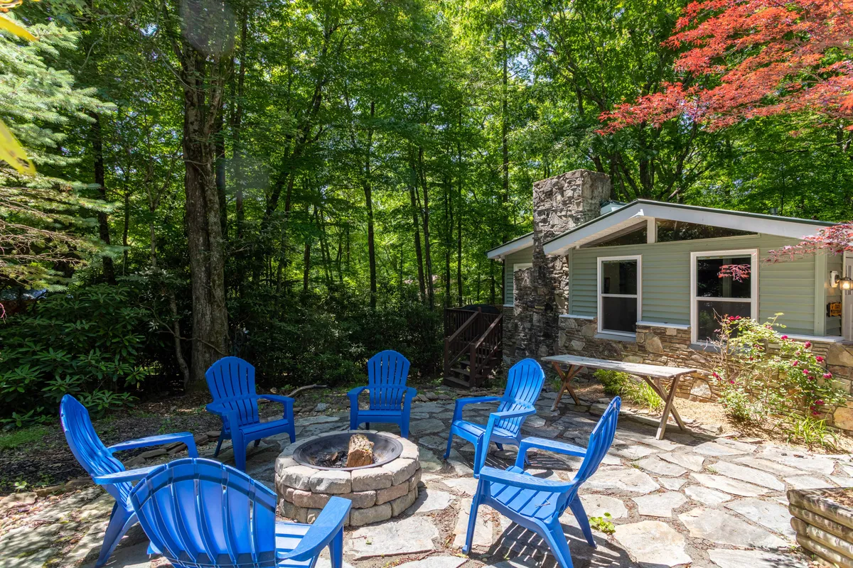 This exterior image captures a cozy fire pit surrounded by blue chairs and a rustic stone wall. The setup is inviting for campfire gatherings, with the fire pit as the focal point, offering a glimpse of the serene natural surroundings.